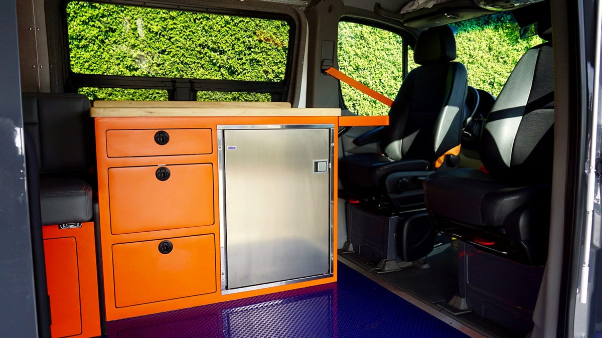 American Van Works custom van with swiveled seats and custom orange galley with wood counter and stainless fridge.