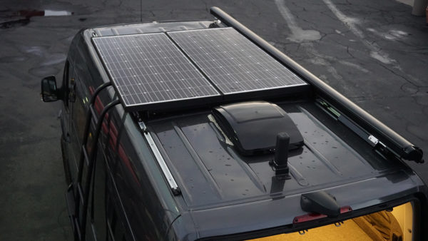 Upfitted van with ladder rack, solar power system, and retractable awning.