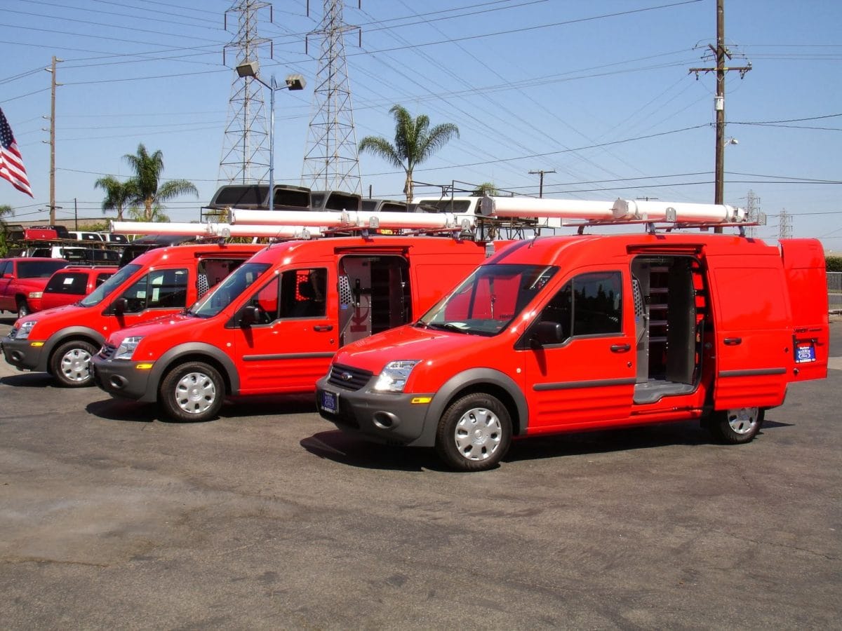 Work fleet of red vans featuring shelving for cargo van by Ranger and white tube racks on top.