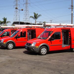 Work fleet of red vans featuring shelving for cargo van by Ranger and white tube racks on top.