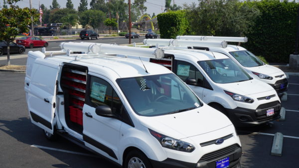 Fleet of three white Ford vans with roof-mounted tube carriers and interior shelving — part of our Work Trucks and Vans solutions.