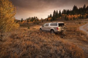 Ford F-150 recreational truck with Leer 100XQ camper shell, hunter in camouflage opening the rear hatch, parked off-road in fall-colored backcountry.
