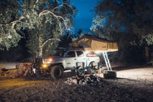 Adventure-ready truck with rooftop tent and RIGID LED lighting creating a cozy illuminated campsite.