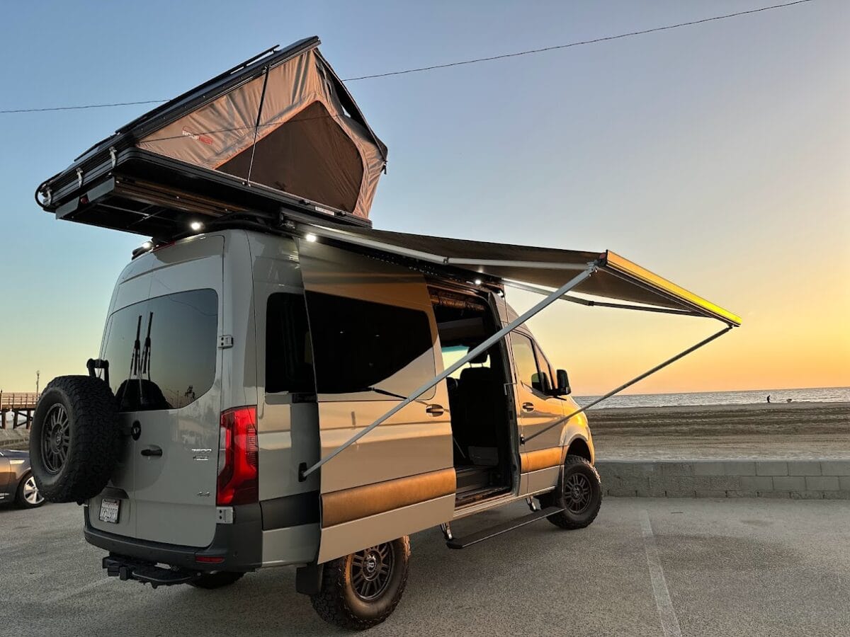 Rooftop tent and awning set up on a recreational truck and van parked at the beach.