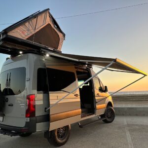 Rooftop tent and awning set up on a recreational truck and van parked at the beach.