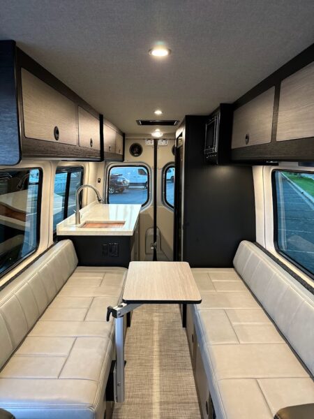 Custom camper van interior with fold-up table, galley, sofa bed, and rear kitchen setup.