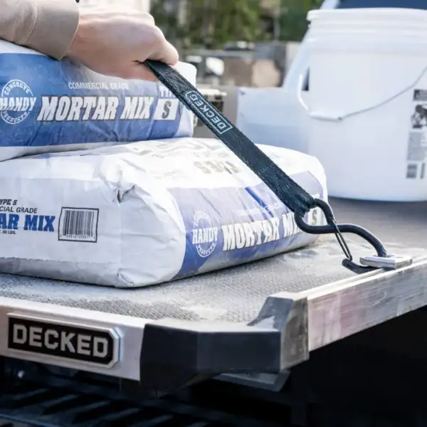 Close-up of DECKED CargoGlide slide at a construction site with tie-down strap securing mortar bags.