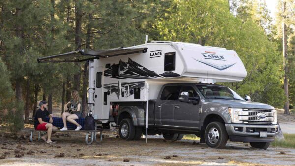 Two young campers in front of a Lance brand Truck Camper in the American wilderness.
