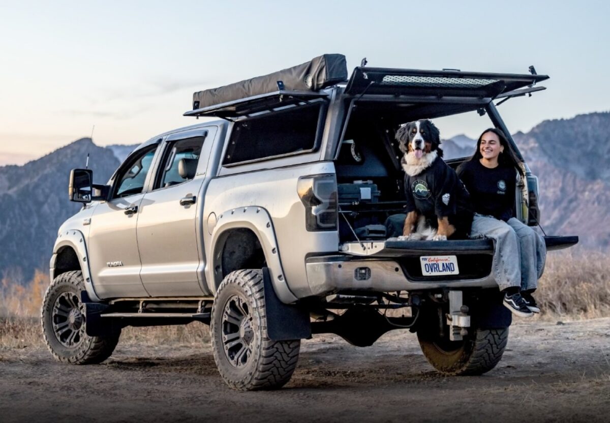 Toyota Tundra with Overland Vehicle Systems Truck Topper with Windows Open and Dog and Driver Sitting on Tailgate