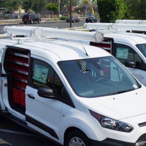Fleet of White Plumbing Vans with Roof Mount Tube Carrier.