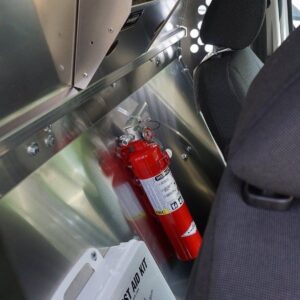 Plumber van interior showing bulkhead partition with mounted fire extinguisher and first aid kit behind cab