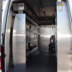 Plumbing van interior with heavy equipment secured near bulkhead and Ranger Design shelving along side wall