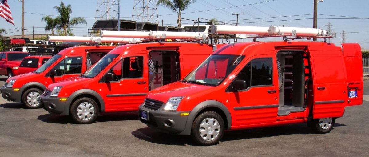 Three red plumbing vans with open side doors showing shelving, drawers, and rooftop tube racks, illustrating organized and efficient plumbing van upfits.