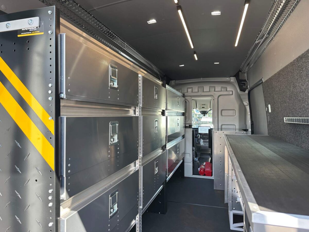 Full interior view of locksmith van upfit showing shelving, workbench, lighting, flooring, and open partition to cab