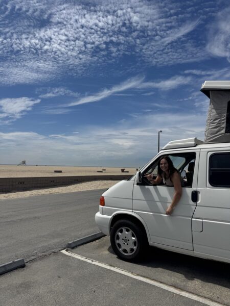 Gabby smiling from the driver’s window of her Volkswagen Eurovan near the beach