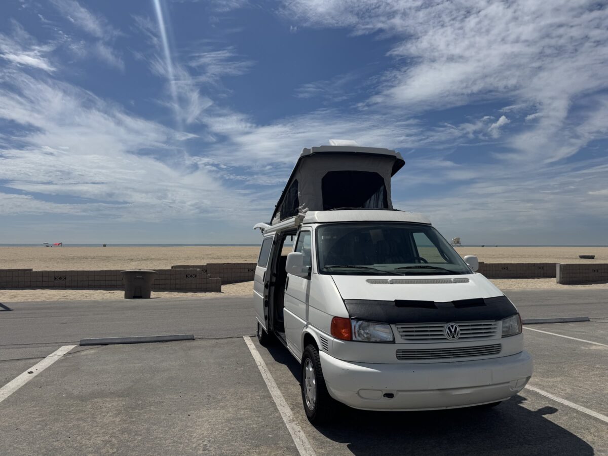 Gabby’s white Volkswagen Eurovan with raised pop-top parked near the beach